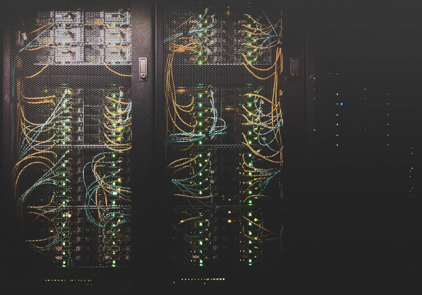 computer servers in a dark server closet with dozens of orange and blue network cables and green lights